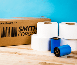 A couple of large white labels rolls stacked on one another in front of a Smith Corona package