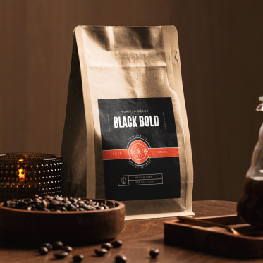 a labeled bag of coffee on a wooden table, to the left of the bag is a lit candle, a shallow bowl overflowing with coffee beans, to the right is a half-full glass pot of coffee sitting on a wooden tray