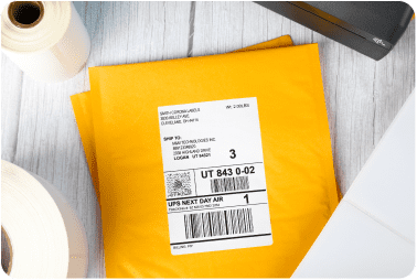 Manilla envelopes with shipping labels affixed sitting laying next to rolls of blank labels