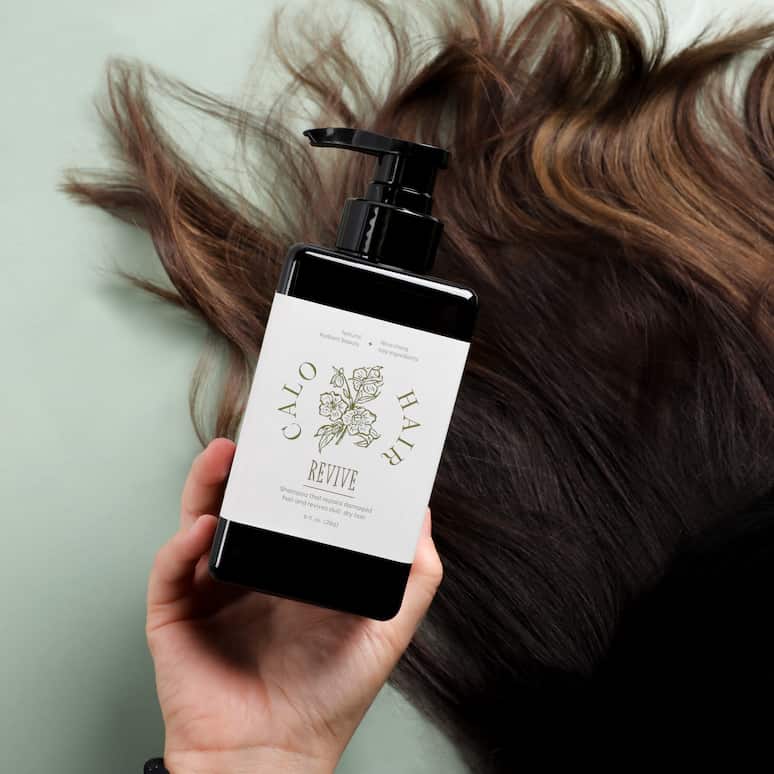 a hand holding a bottle of shampoo next to someones hair splayed down on the floor