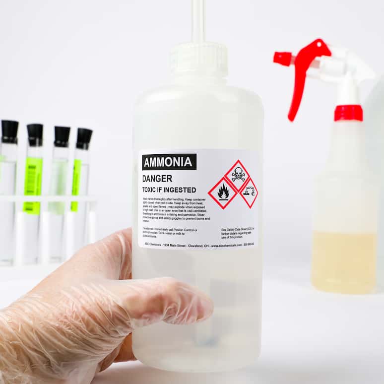 a gloved hand holding a bottle of ammonia with test tubes and other chemicals in the background