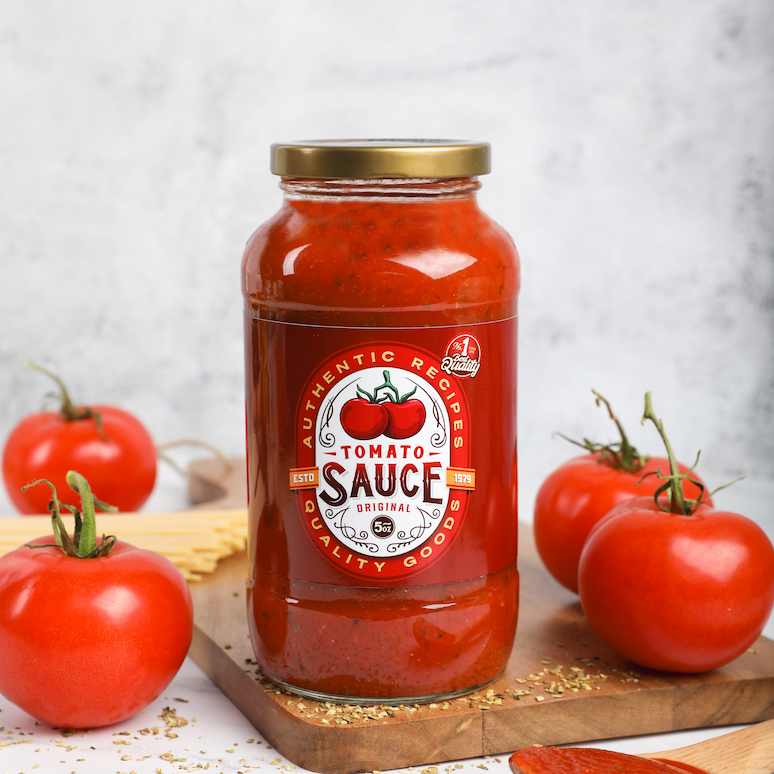 a jar of tomato sauce on a cutting board, flanked by two tomatoes on each side, a spoonful of sauce sits in the foreground