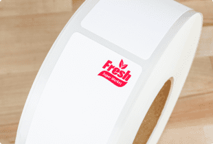 A roll of scale labels viewed from top down with a red brand logo in the upper right hand corner of the label