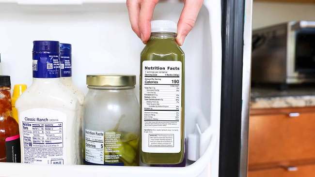 a hand pulling a bottle of juice off of a fridge shelf with the nutrition label facing out