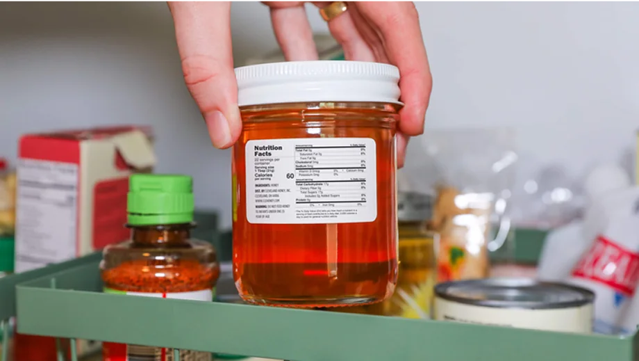 a hand pulling a labeled jar of honey from a fridge shelf