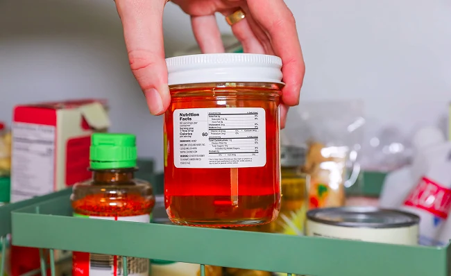 a hand pulling a honey jar out of a fridge with the nutrition label facing out