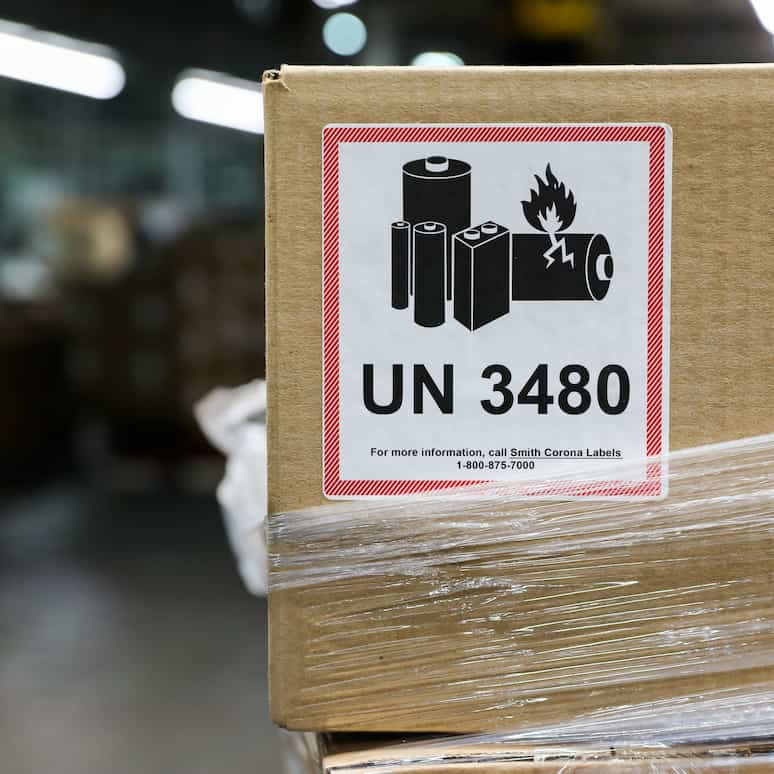 a UN 3480 label on a cardbox in a factory, the box is partially wrapped with plastic