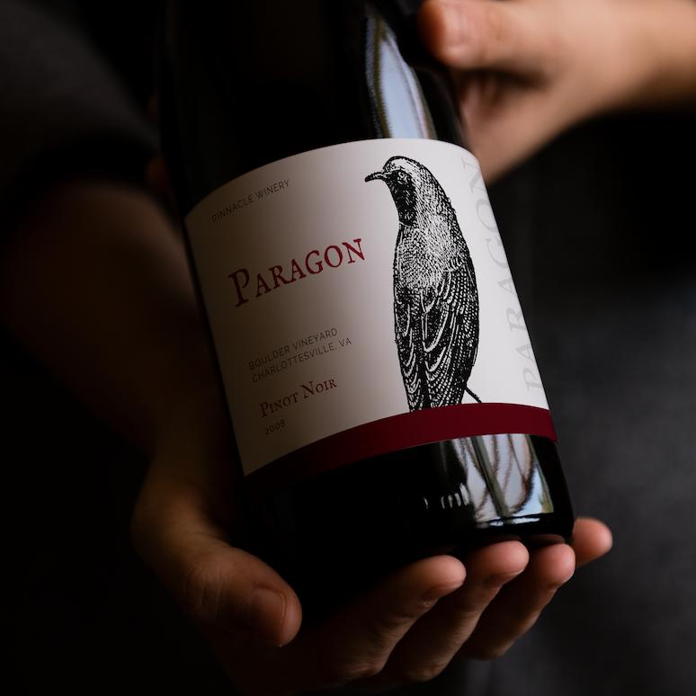 two hands holding a bottle of pinot noir with one of the hands supporting it from the bottom