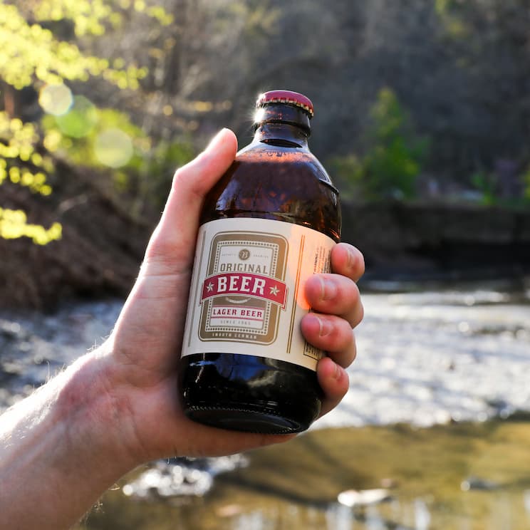 a hand holding a bottle of lager in the wilderness