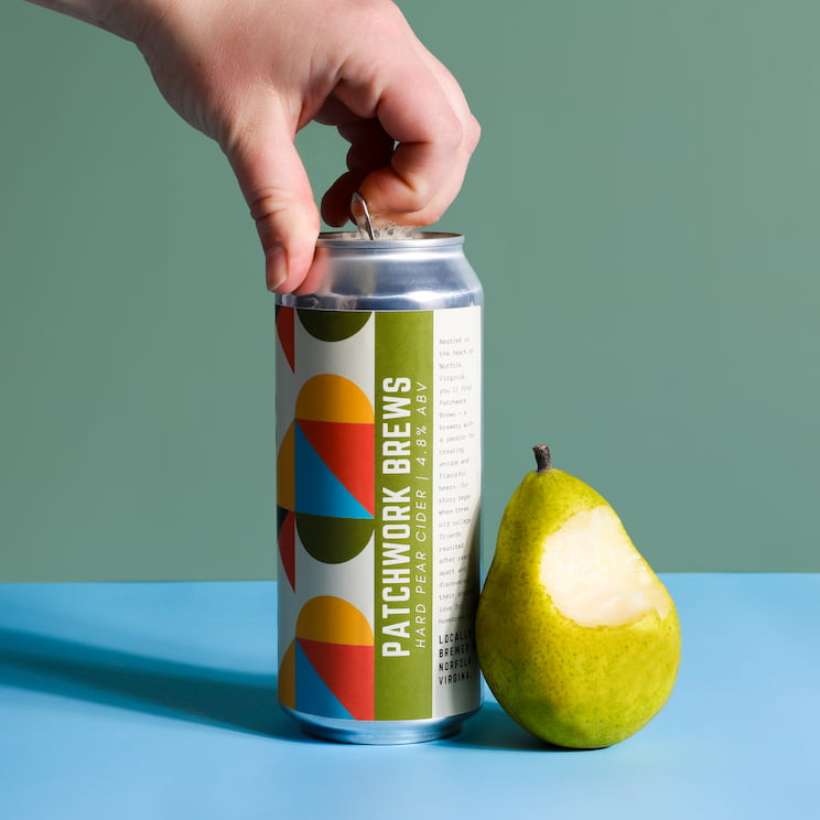 a hand cracking open a can of pear cider, a bitten pear is leaning on the can