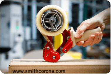 A hand using a tape applying device to seal a cardboard package
