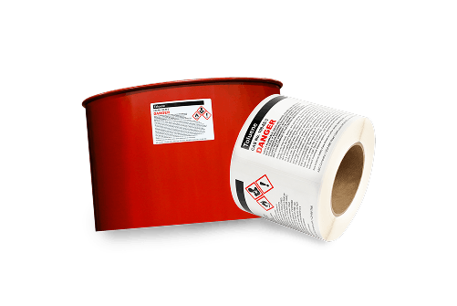a labeled chemical drum next to a roll of ghs labels