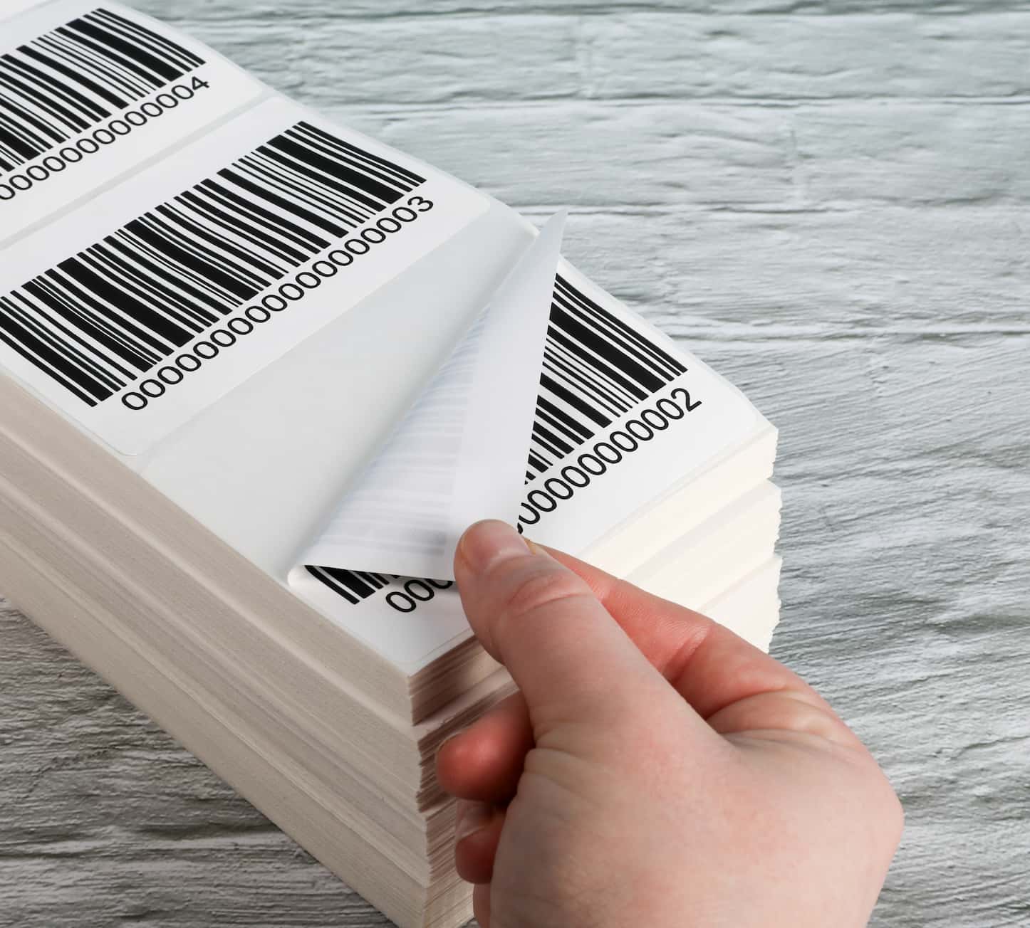 a hand peeling off a barcode label from a stack of fanfold labels