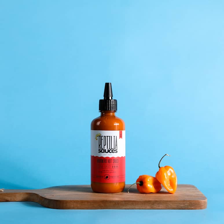 a cutting board holds a bottle of habanero hot sauce and two habanero peppers