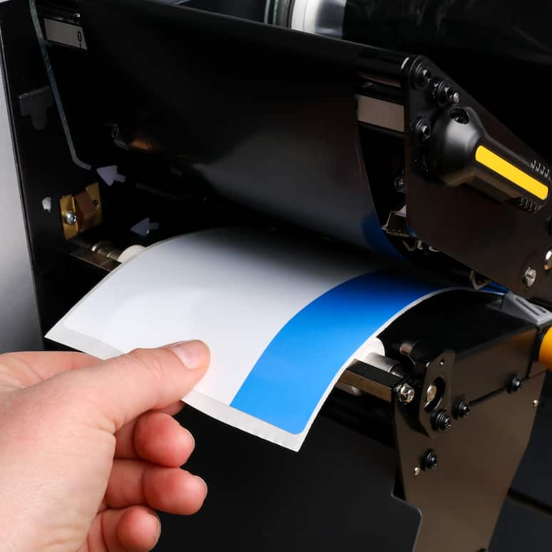 a hand pulling a label out of a printing machine
