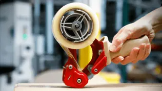 A hand using a tape applying device to seal a cardboard package